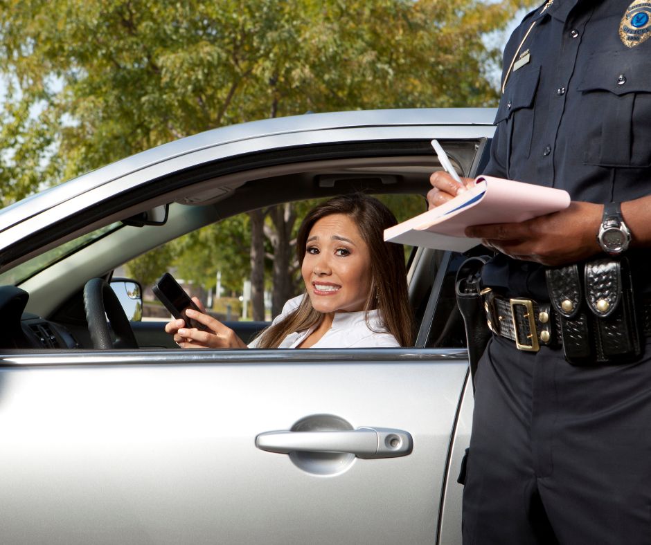 Driver looks at camera as police officer writes traffic ticket that will add points and penalties